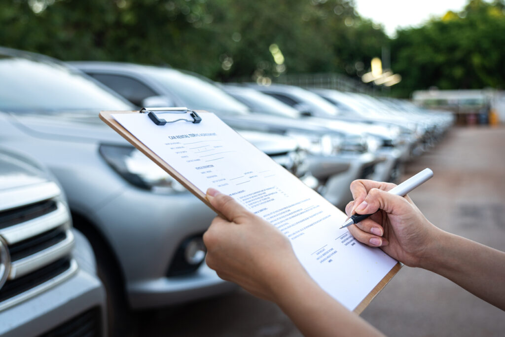 pessoa fazendo checklist na frente de carros estacionados com imagem borrada ao fundo